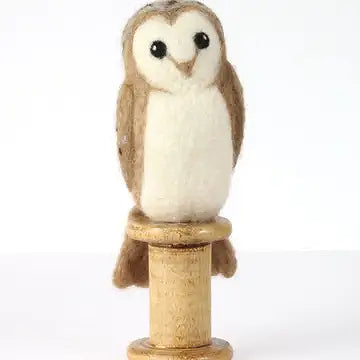 Small needle felted owl figurine on a wooden base against a white background