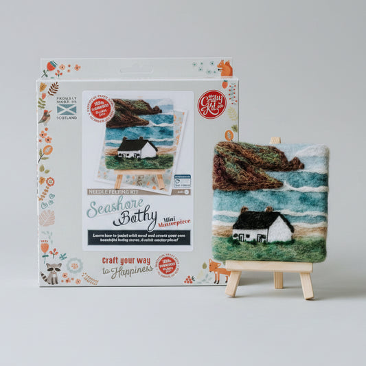 Craft kit packaging with a small needle felted artwork on an easel against a blurred background