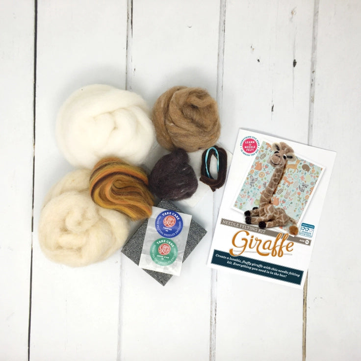Felted wool balls and a craft kit for making a giraffe on a white wooden surface