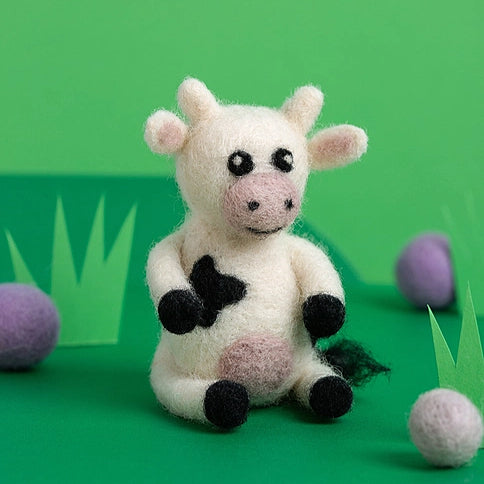 Small needle felted cow  on a green background with grass and felted balls