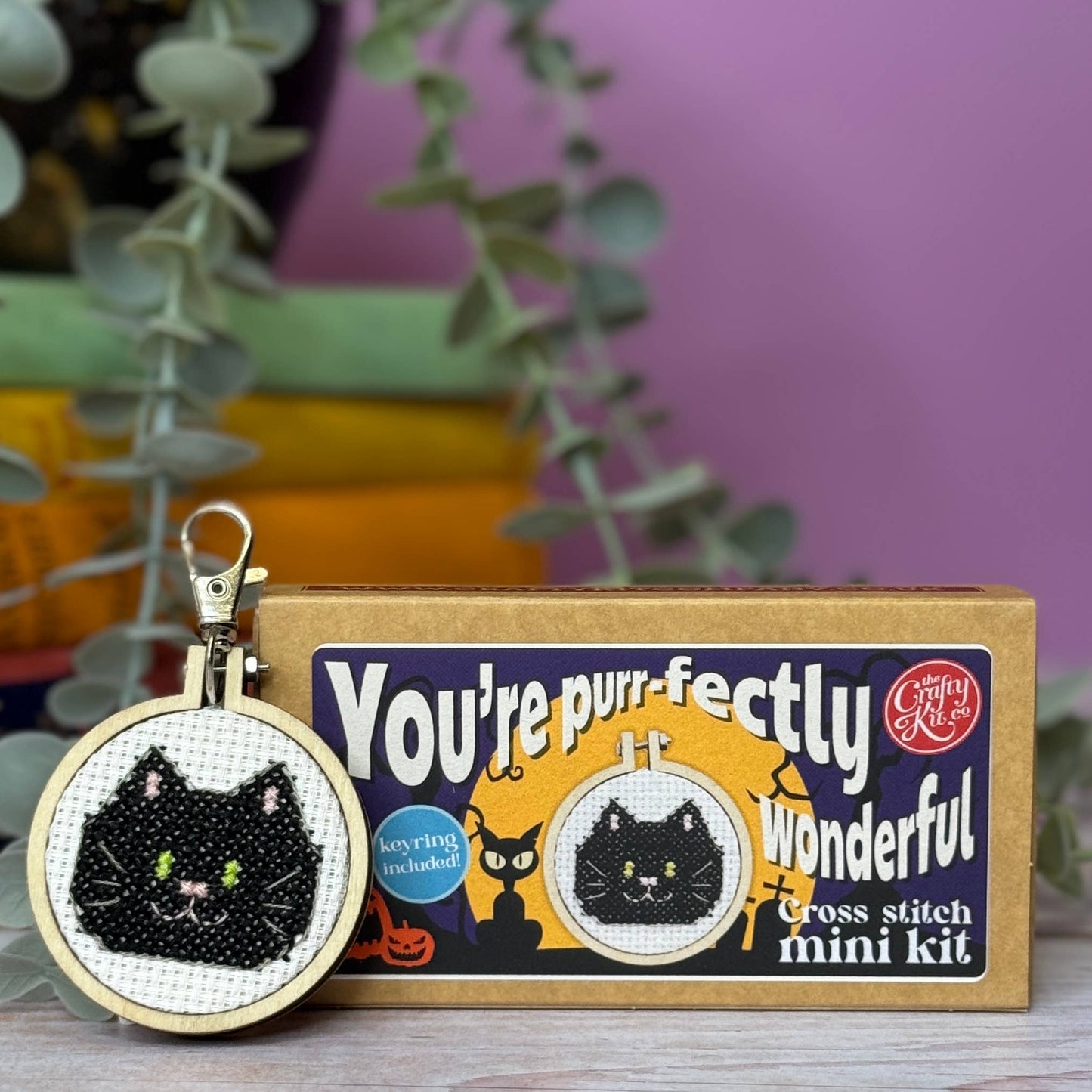 Cross-stitch keychain with black cat design and packaging labeled 'You're purr-fectly wonderful' on a blurred background.