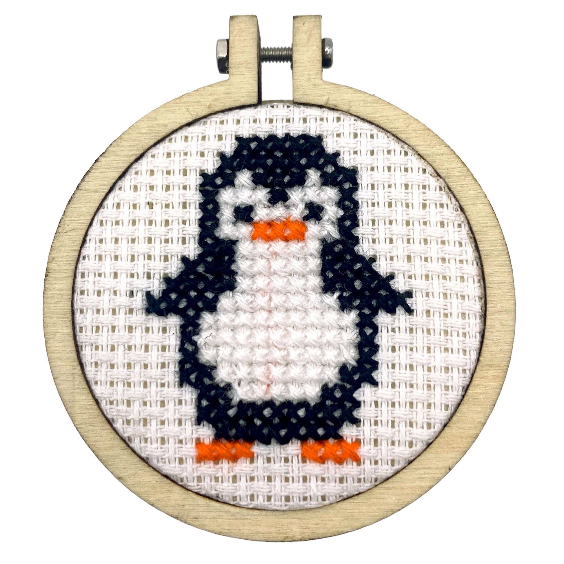 Cross-stitched penguin in an embroidery hoop on a white background