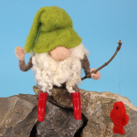 Gnome figurine with a green hat and red boots sitting on a rock against a blue background.