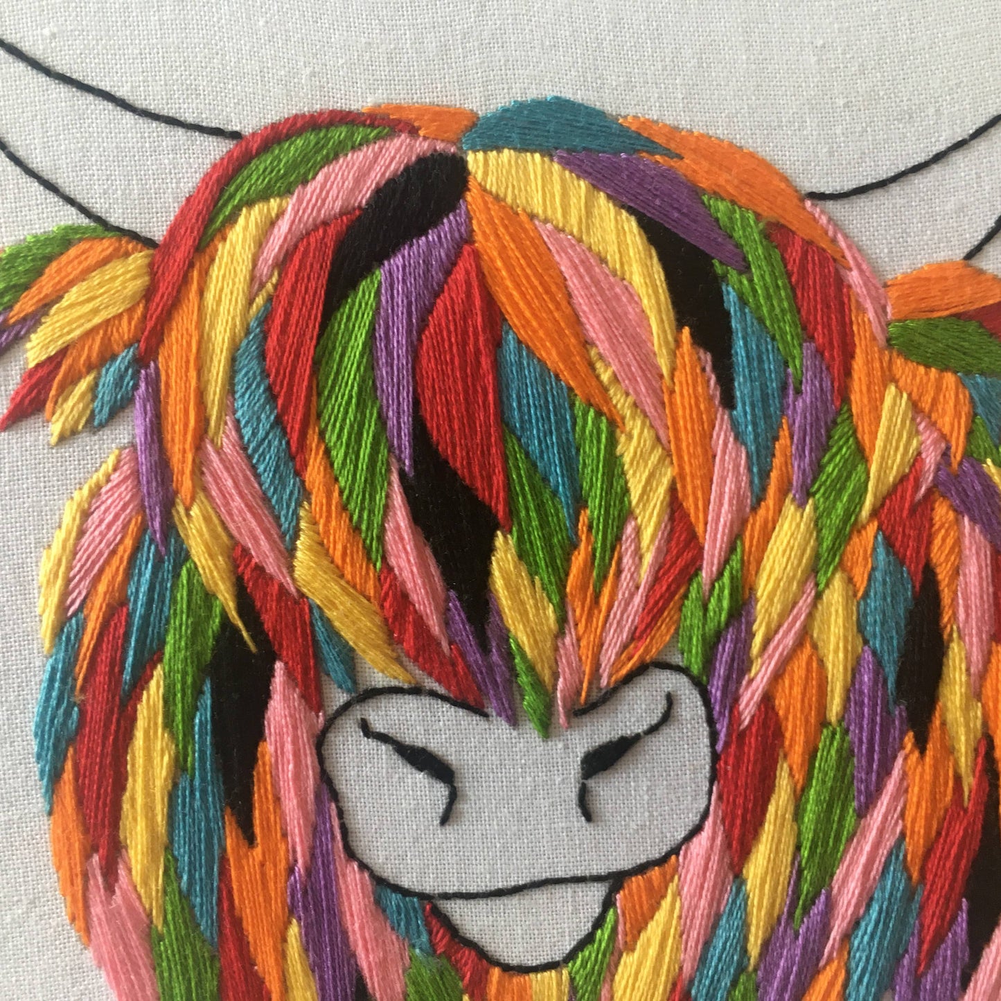 Embroidered cow with colourful hair and a neutral expression on a light background