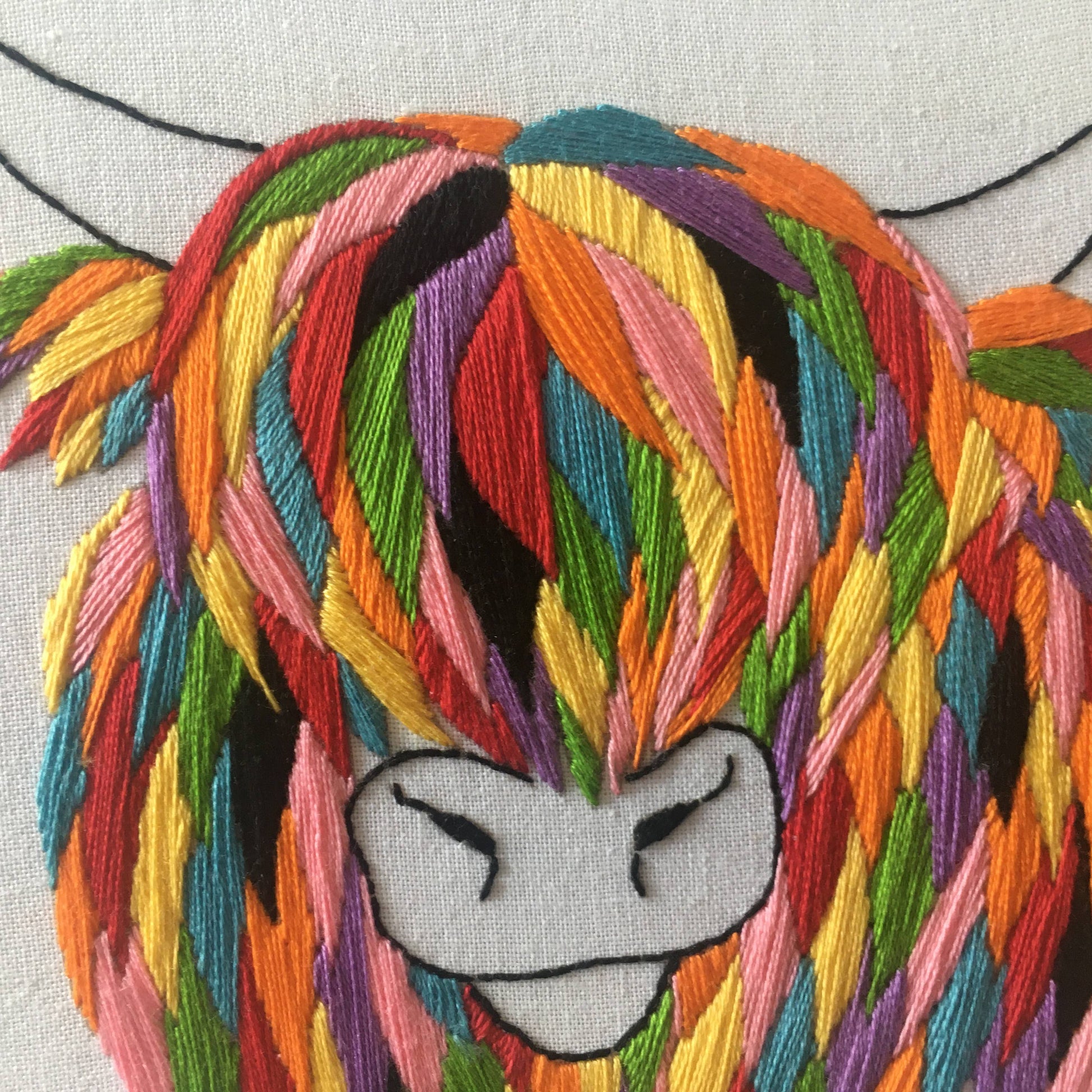 Embroidered cow with colourful hair and a neutral expression on a light background