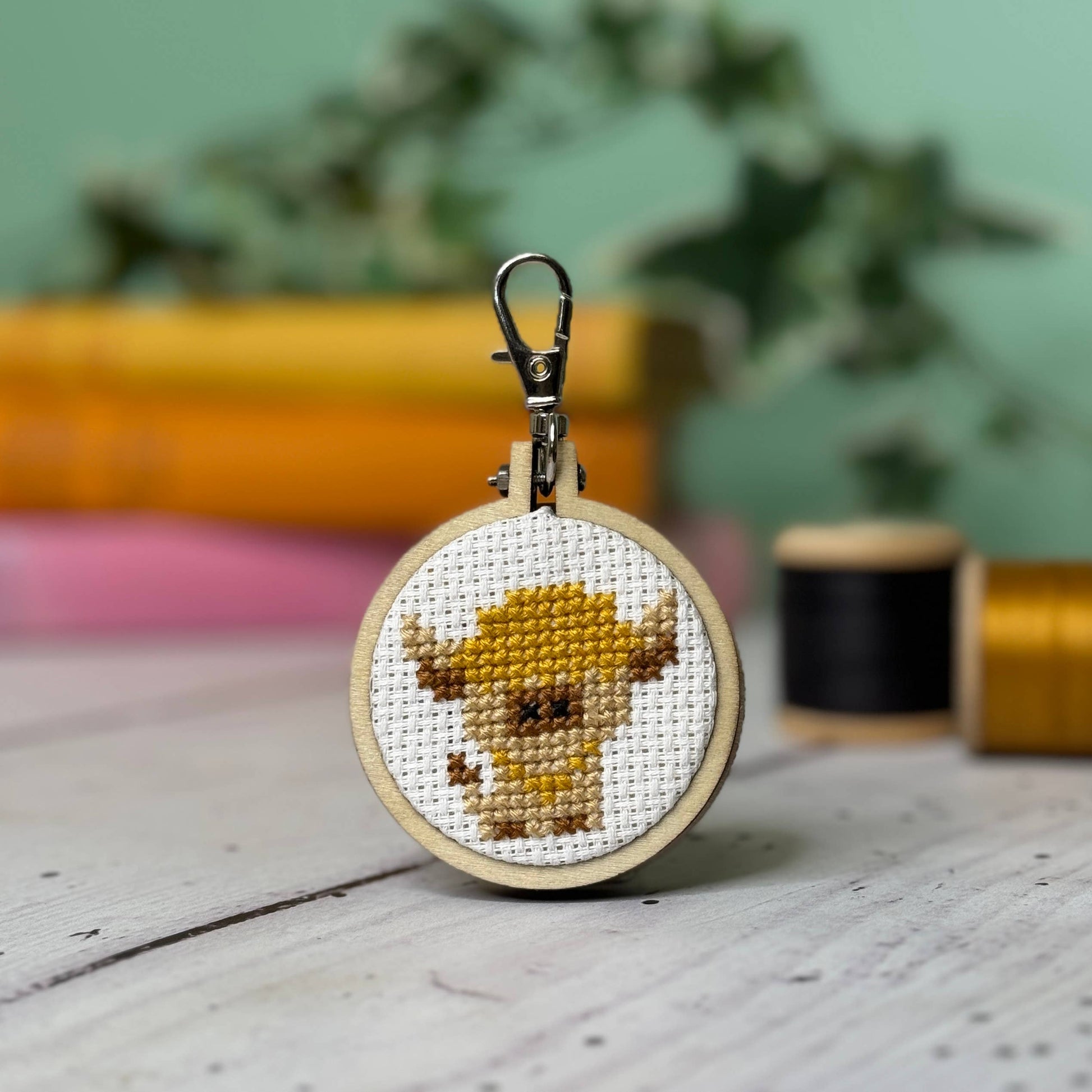 Cross-stitched keychain with a cow design on a wooden surface.