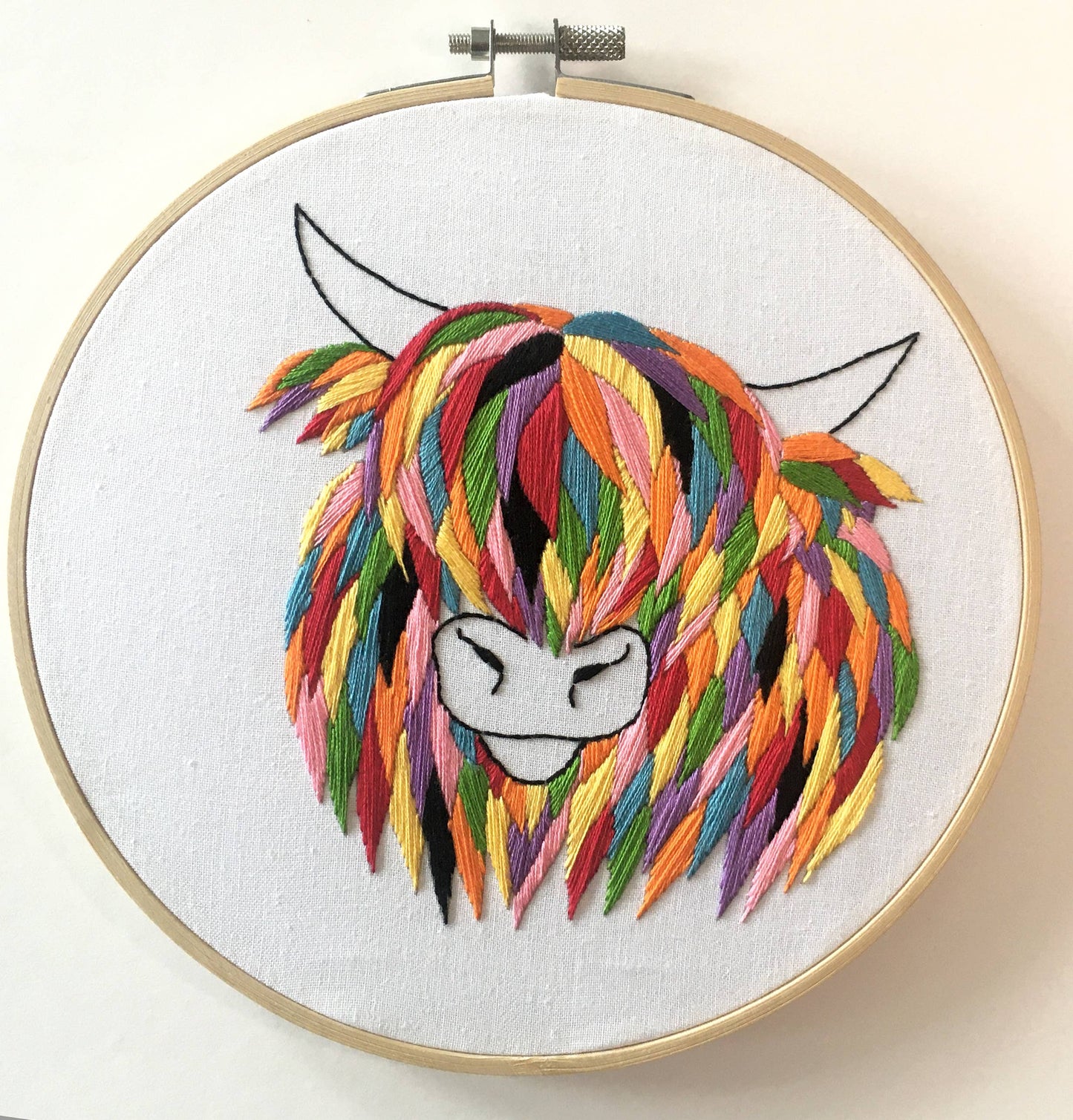 Embroidery hoop with a colourful embroidered design of a highland cow.