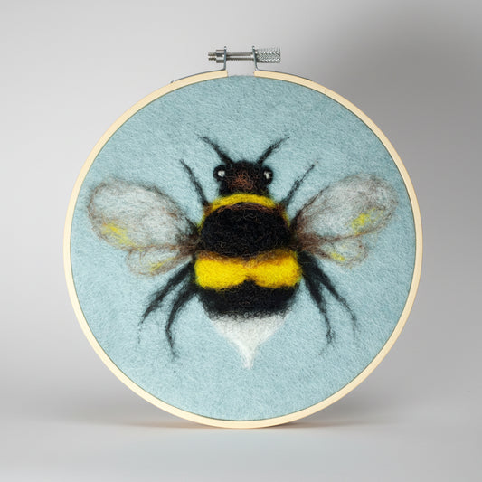 Embroidery hoop with a felted bee design on a light blue background