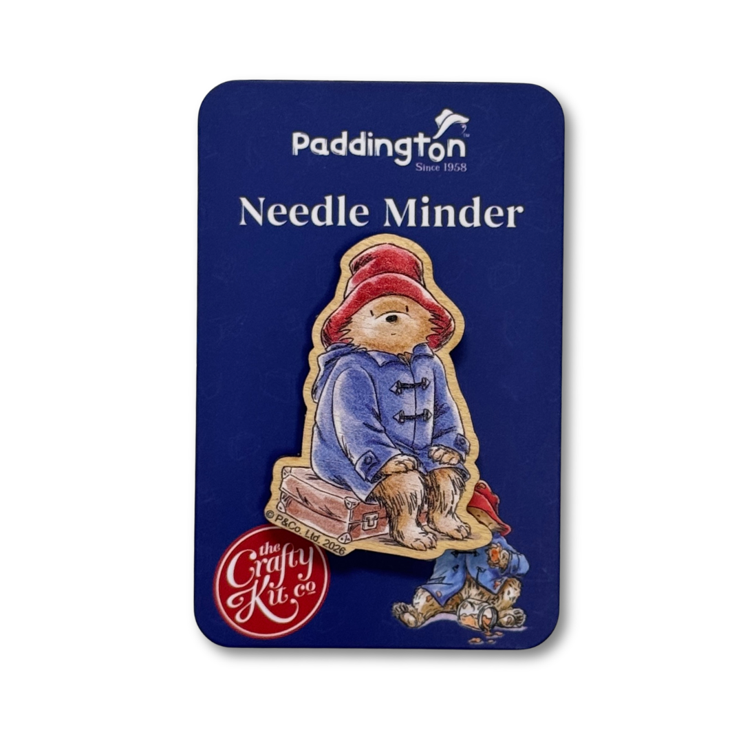 Paddington 'Needle Minder' enamel pin by The Crafty Kit Co, mounted on its original dark blue backing card. The pin depicts Paddington Bear wearing his signature red hat and blue duffel coat.