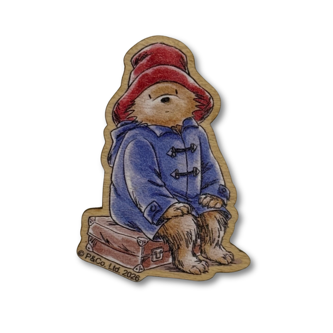 A die-cut wooden needle minder featuring an illustrated bear wearing a red hat and blue duffel coat, sitting on a suitcase. The artwork has visible wood grain edges, and a small copyright mark reading 'PACO LTD 2008' appears near the bottom left.