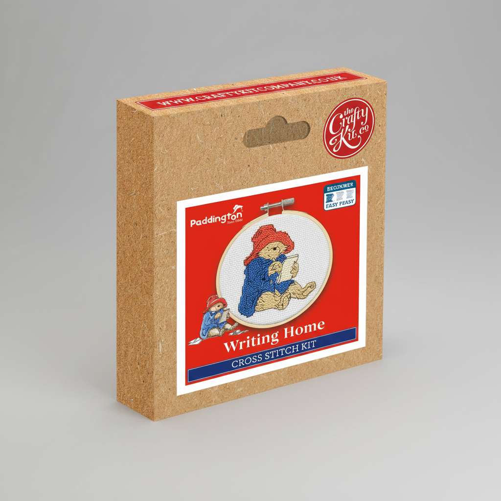 Paddington cross stitch kit in its original brown cardboard box packaging, featuring a red front label with an illustration of Paddington writing and the text 'Writing Home Cross Stitch Kit'.