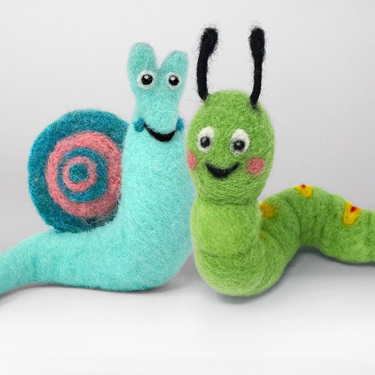 Two handmade felt wool animal toys, a light blue snail with a pink and blue spiral shell and a green caterpillar with black antennae and small yellow spots, set against a plain light grey background.