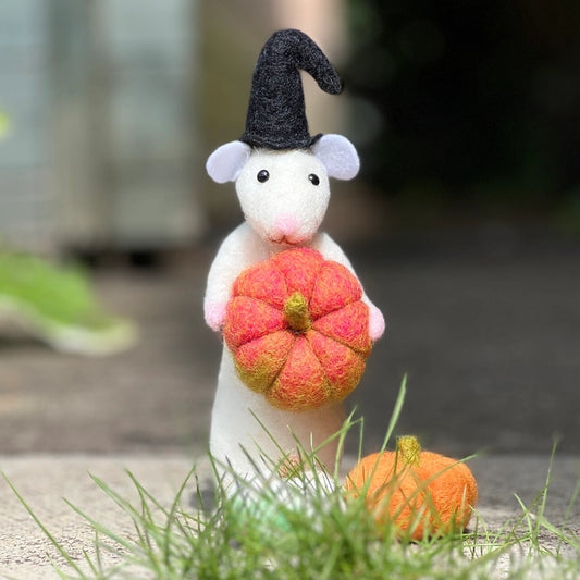 Felted mouse wearing a witch hat holding a felt pumpkin in a natural setting.